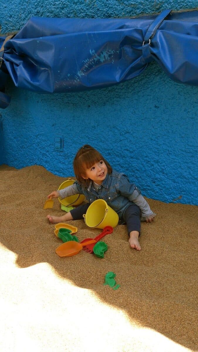Niña pequeña sentada en el arenero rodeada de moldes de colores