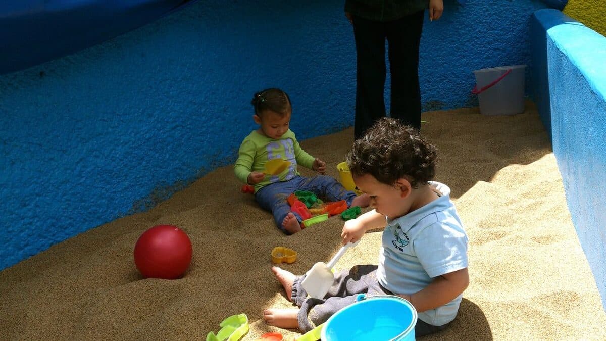 Dos niños pequeños juegan con cubetas y una pelota en el arenero