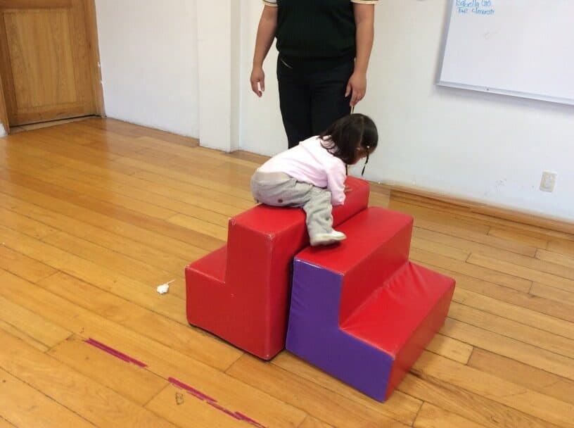 Niña pequeña gatea sobre la rampa de espuma roja y morada durante su clase de psicomotricidad
