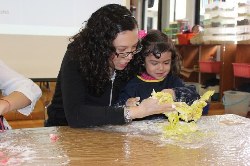 Maestra y alumna juegan con gel sensorial amarillo sobre una mesa cubierta con plástico