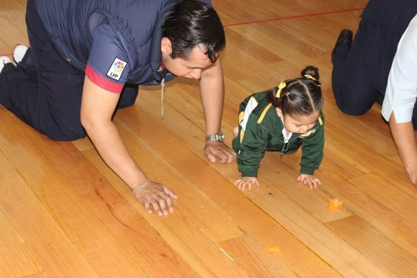 Maestra gatea junto a una alumna en uniforme para mostrarle el ejercicio