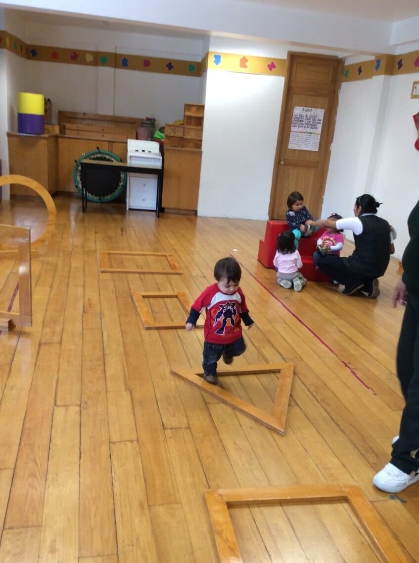 Niño pequeño camina dentro de un marco cuadrado de madera colocado en el piso del salón