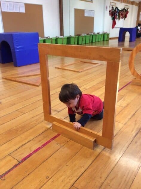 Niño con suéter rojo cruza el marco de madera visto desde el otro lado del salón