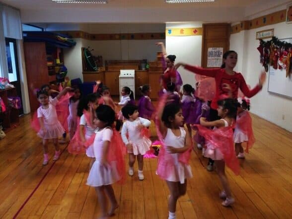 Maestra de ballet marca un movimiento con los brazos y las alumnas la siguen