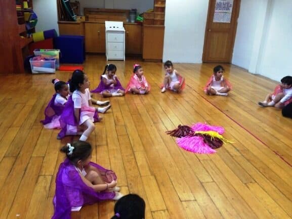 Alumnas con tutús rosas y morados descansan sentadas al final de la clase de ballet