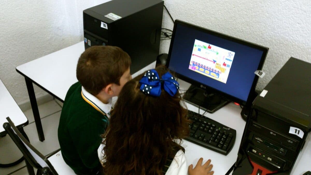 Dos alumnos frente a una computadora con un programa didáctico en pantalla