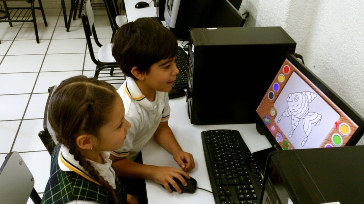 Dos alumnos comparten una computadora; una de ellas usa el ratón para dibujar en pantalla