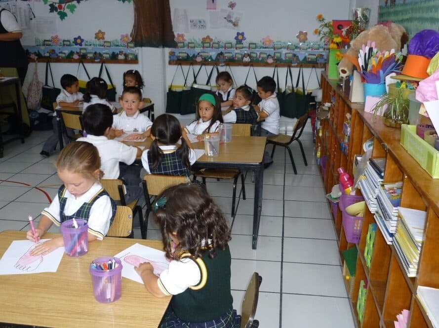 Salón de clases con alumnos trabajando en sus mesas y material didáctico en los estantes