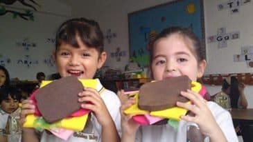 Dos alumnas muestran las hamburguesas de cartón y papel que armaron en clase