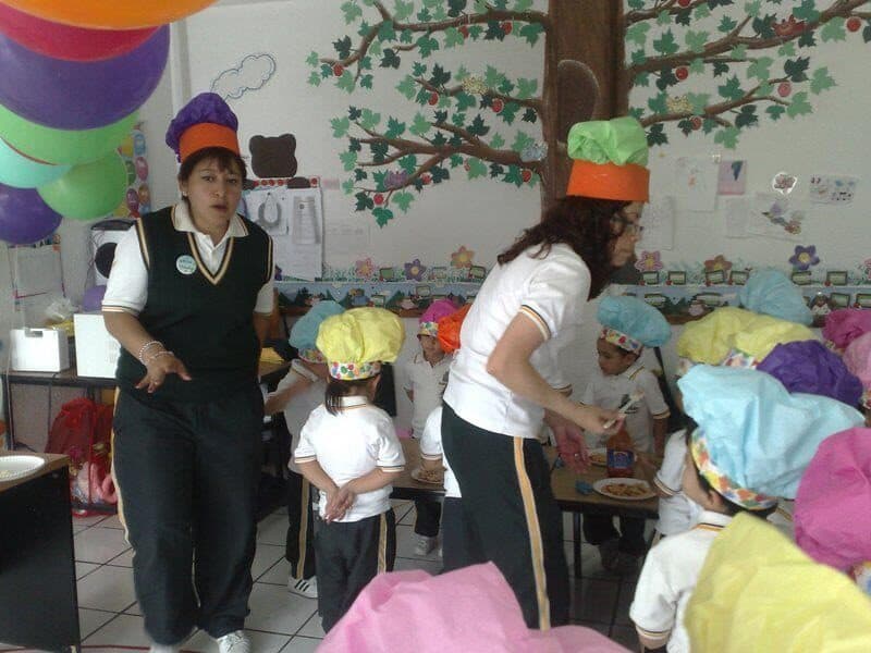 Maestras y alumnos con gorros de cocinero durante el taller de pizza en el salón decorado