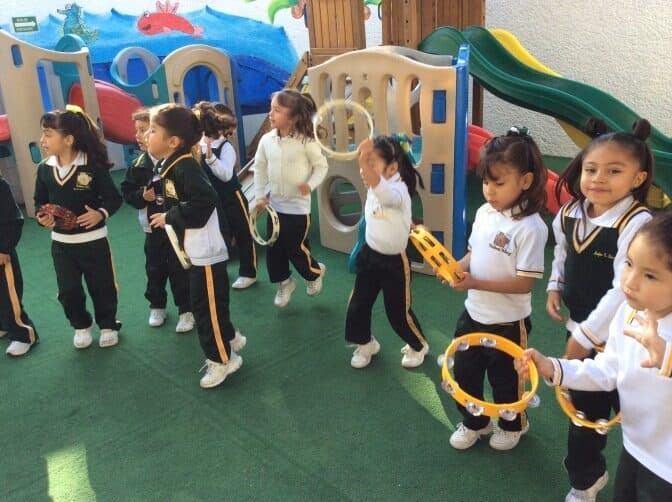 Alumnos con panderos y aros junto a los juegos infantiles del patio