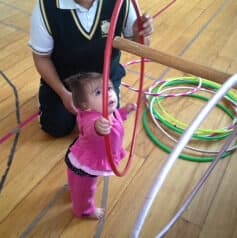 Niña pequeña sostiene un aro mientras su maestra guía el ejercicio con aros de colores