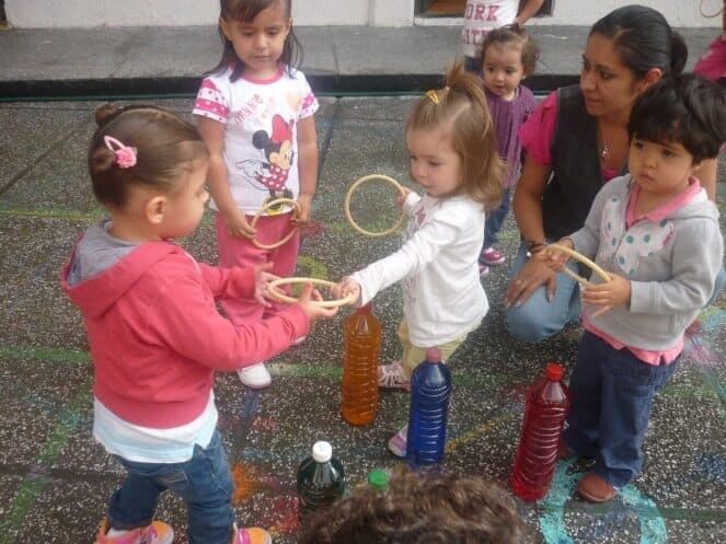 Niños de maternal juegan al aire libre con aros y botellas de colores