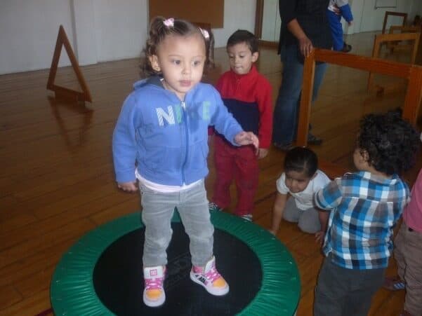Niña pequeña salta sobre un mini trampolín mientras sus compañeros esperan turno