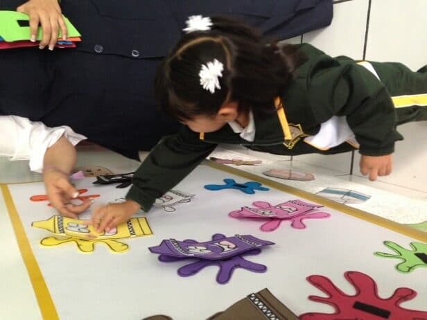 Niña en uniforme acomoda figuras de foami de colores sobre un pliego de papel en el piso