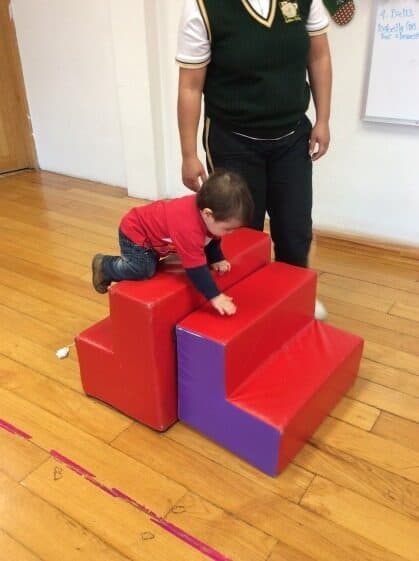 Niño pequeño gatea sobre la rampa de espuma mientras su maestro lo acompaña de pie