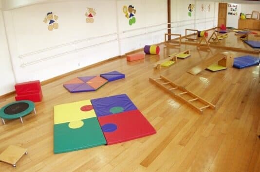 Salón de psicomotricidad con tapetes de rompecabezas, trampolín y escalera de madera