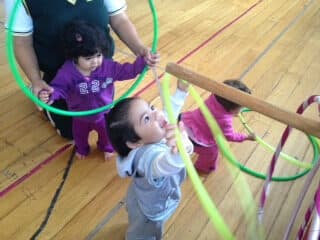 Niños pequeños sostienen aros de colores durante un ejercicio guiado por su maestra