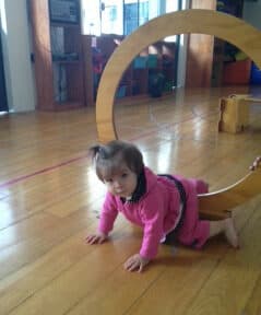 Niña con conjunto rosa gatea bajo un arco de madera del circuito