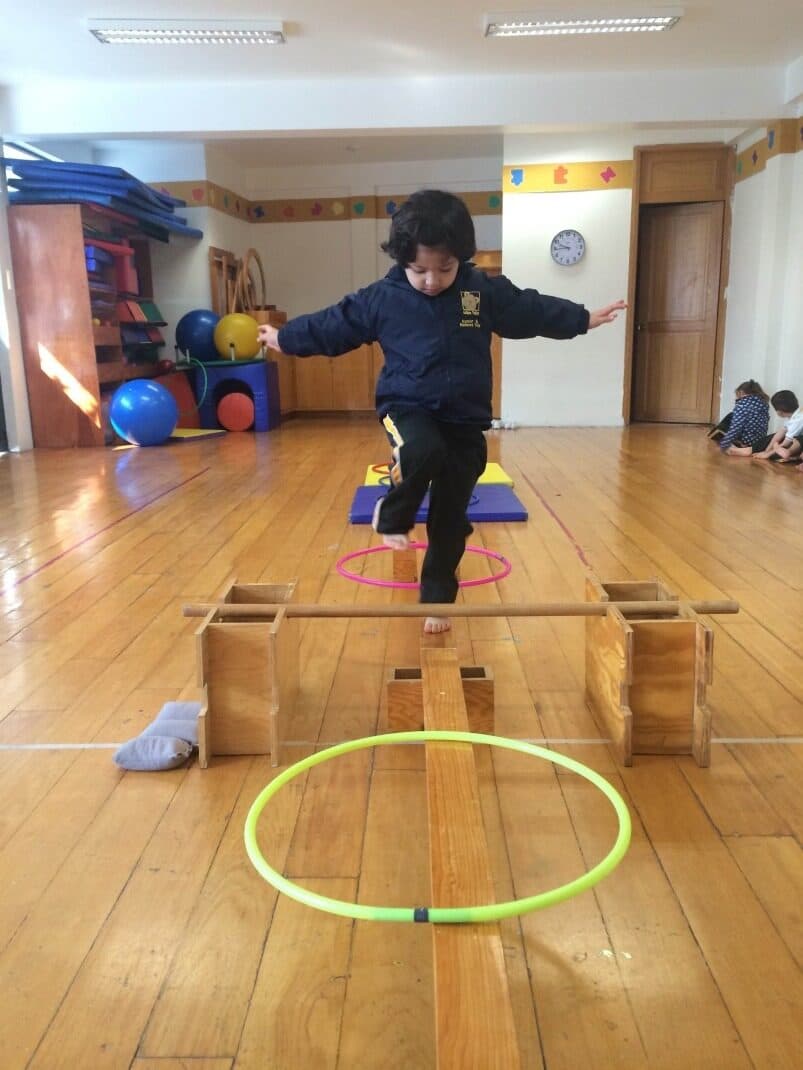 Alumno mantiene el equilibrio con los brazos abiertos sobre la viga de madera