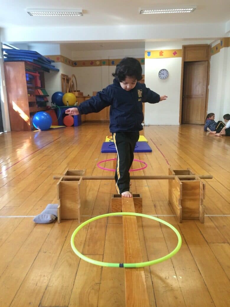Alumno da un paso sobre la viga de equilibrio dentro del circuito de psicomotricidad
