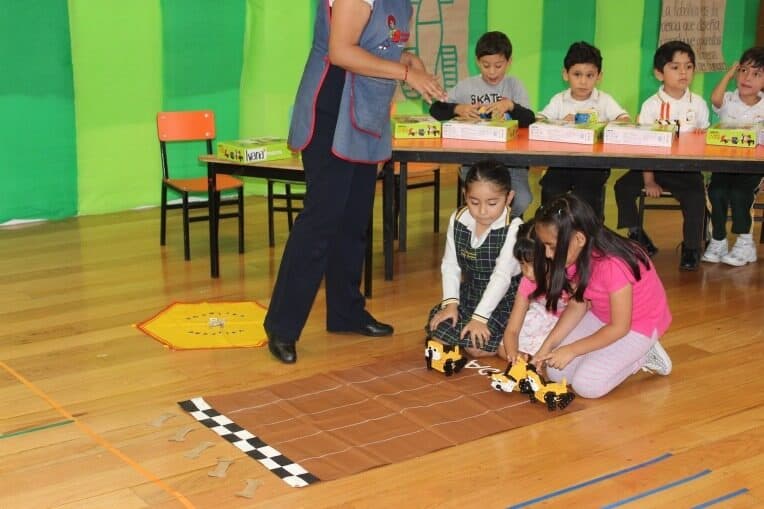 Alumnas colocan un carro robot sobre una pista marcada en el piso mientras el grupo observa