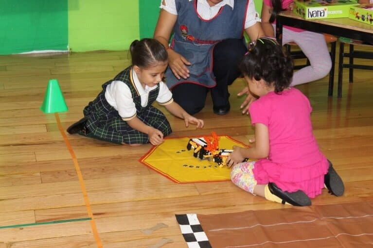 Dos alumnas ajustan su robot armable sobre el tapete de la pista