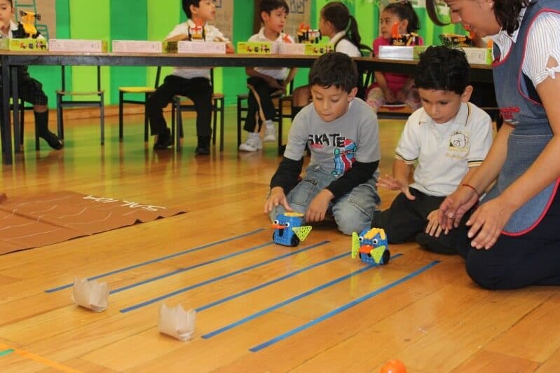 Dos alumnos preparan sus carros robot en los carriles marcados con cinta azul