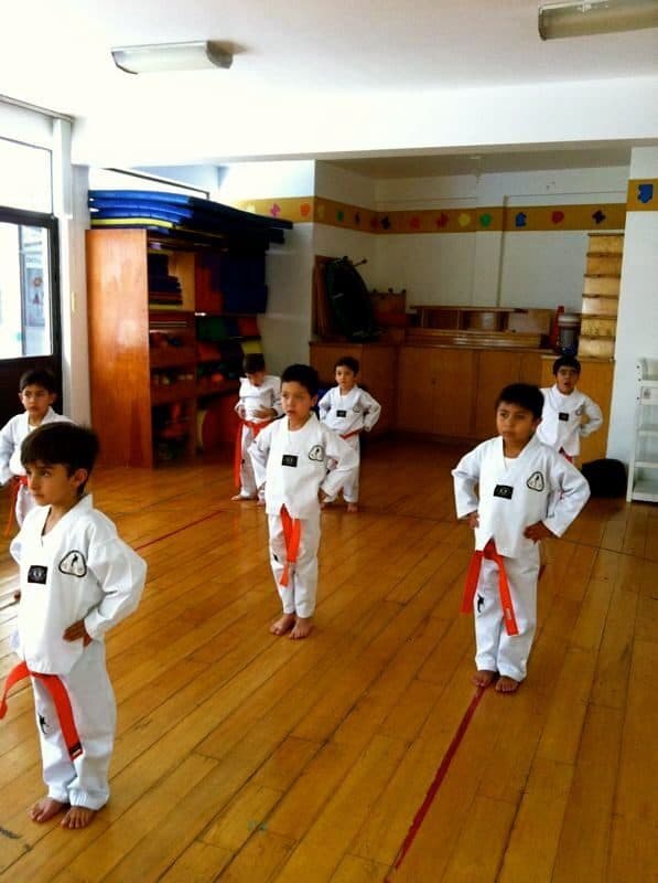 Alumnos con dobok y cinta roja mantienen la posición de guardia en el salón