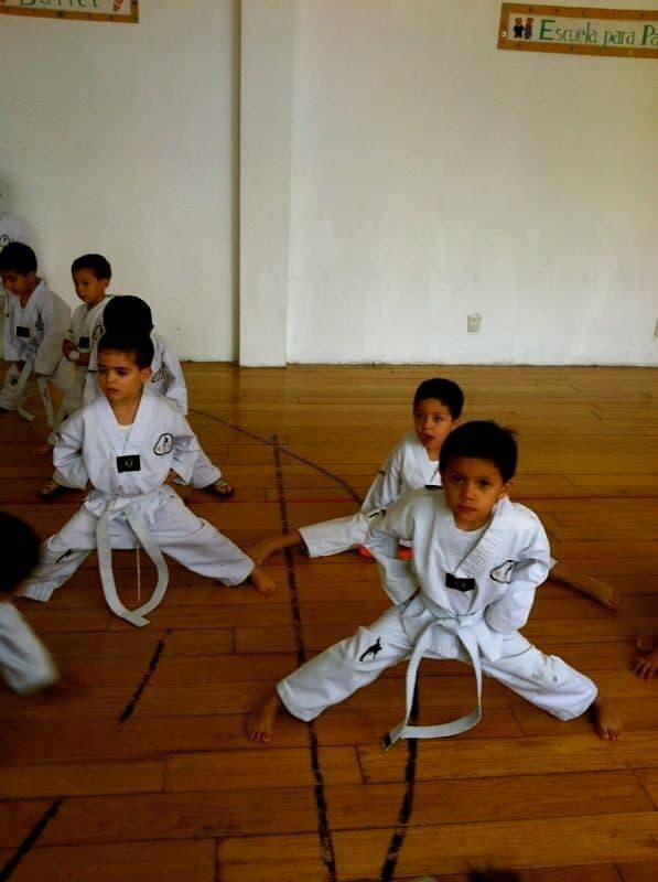 Dos alumnos con dobok sostienen una postura baja de piernas abiertas