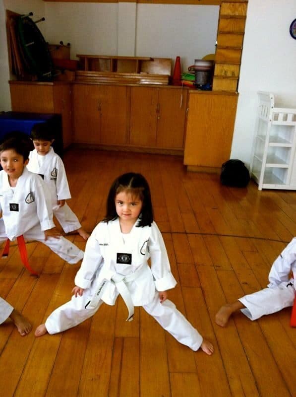 Alumna con dobok blanco y cinta blanca sostiene una postura de piernas abiertas
