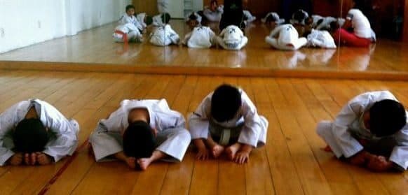Grupo de alumnos con dobok inclinados sobre el piso al cerrar la clase de Tae Kwon Do
